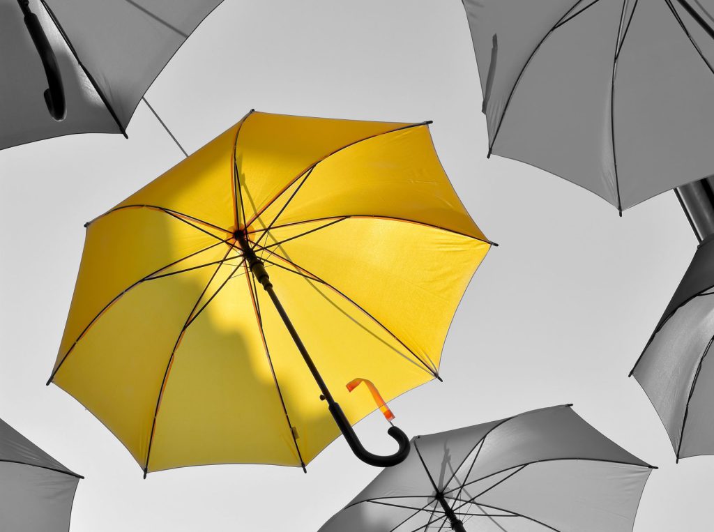 Ein Schwarzweiß Foto, das Regenschirme zeigt. Einer davon ist gelb eingefärbt.